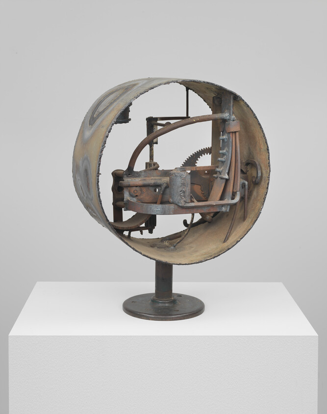 Rusty circular metal sculpture revealing gears and mechanical parts on a pedestal.