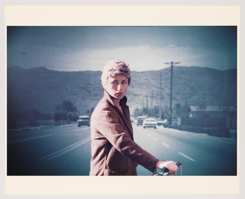 Young person on a bicycle looks back while stopped in the middle of a road with cars.