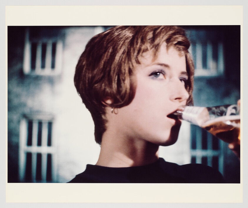Person with short hair drinks from a glass bottle while looking off to the side.