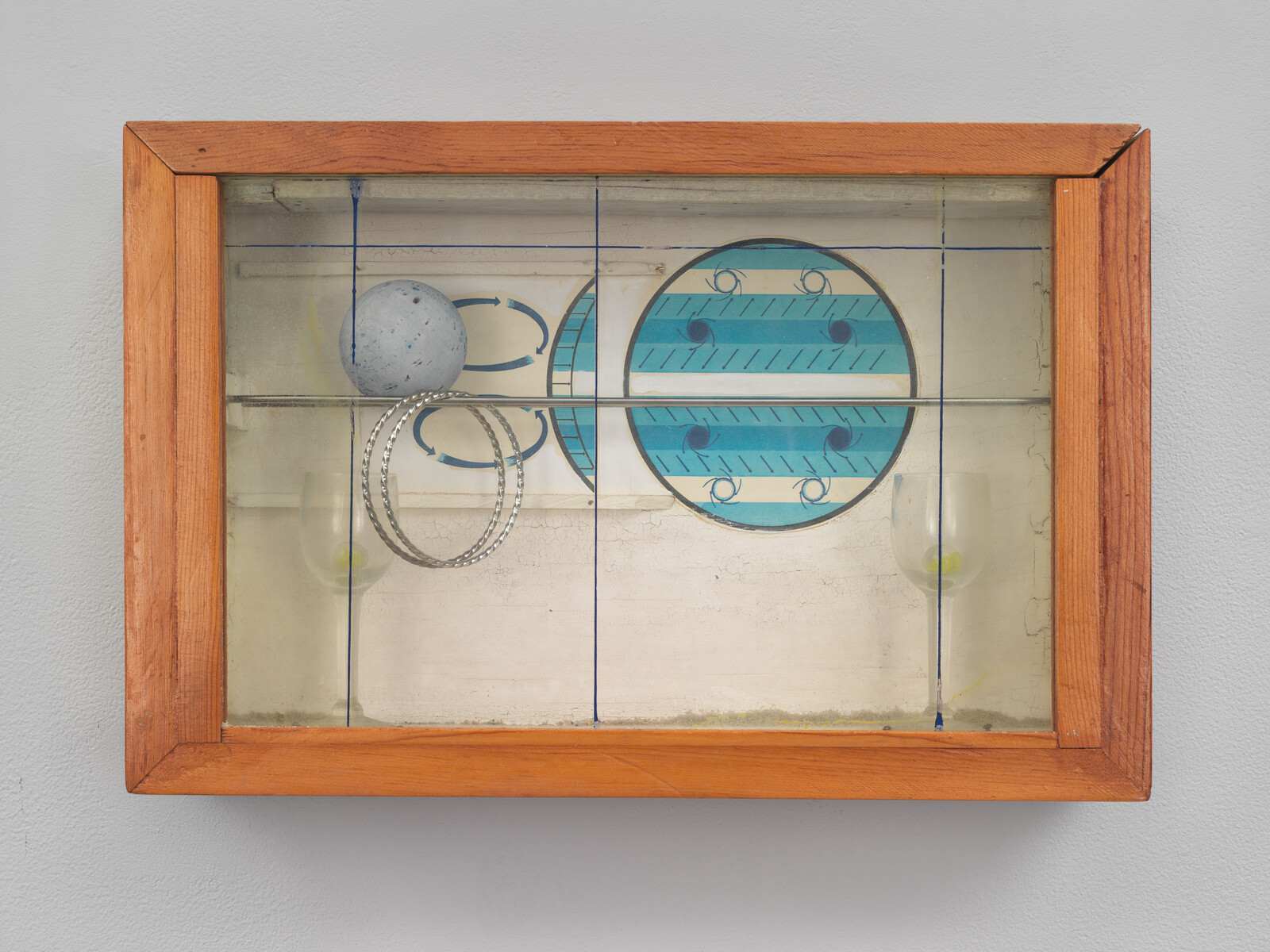 Wooden-framed glass box displays painted blue circles, a gray ball, two metal rings and wine glasses.