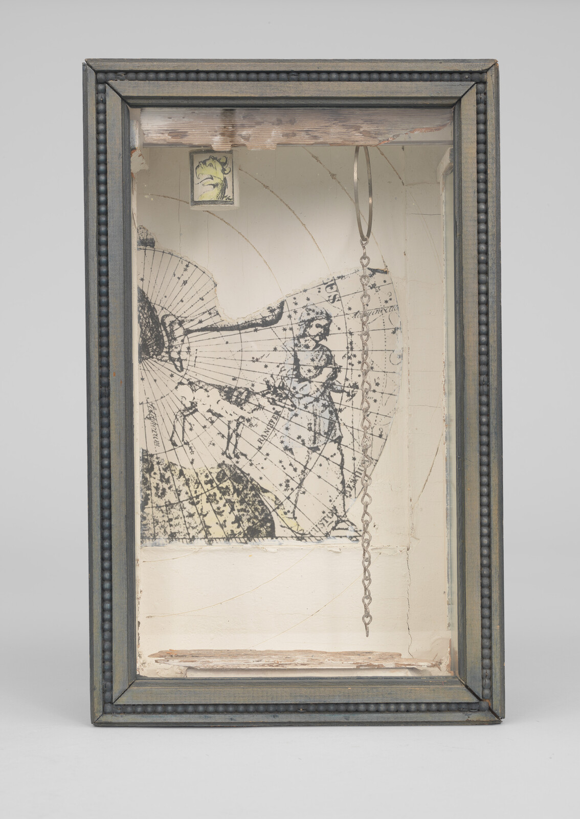 Wooden shadow box containing an old star map print and a dangling metal chain inside.