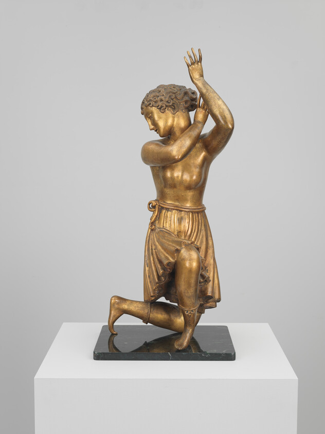 A bronze statue of a kneeling youth with arms raised above his head.