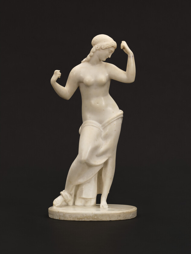 White marble statue of a woman standing, partially draped, with one arm raised and head turned downward.