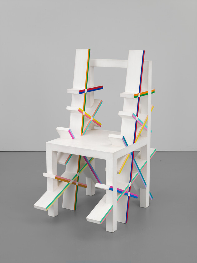 A chunky white wooden chair adorned with colorful striped slats forming X-shaped braces and accents.