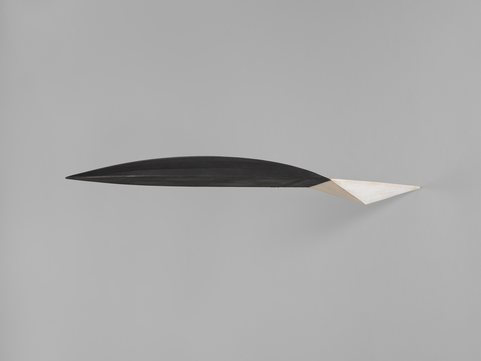 Long black wall sculpture with a white triangular tip mounted on a gray wall.