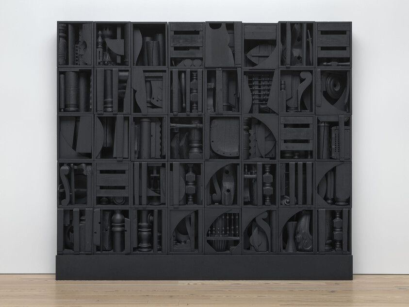 Large black wooden cabinet with many square compartments, each filled with various dark, abstract wooden objects and shapes.