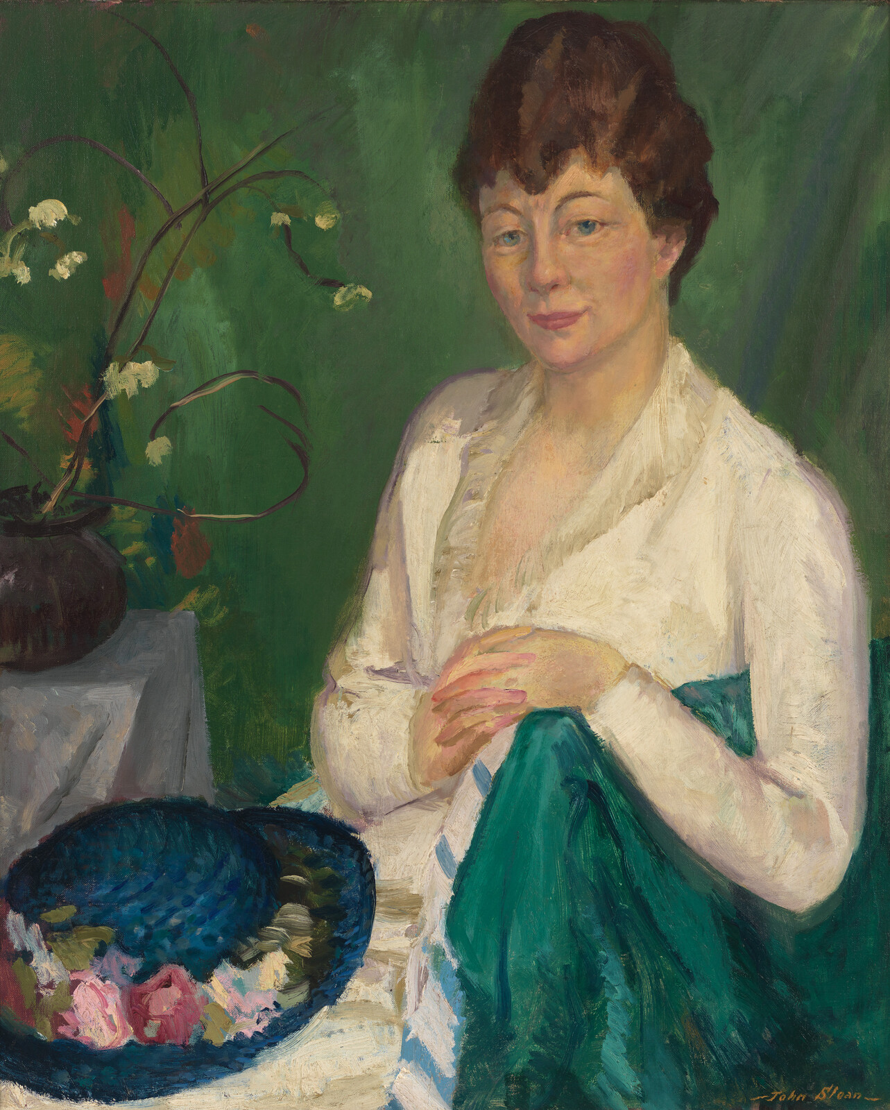 A seated woman in a white blouse holds a green cloth beside a bowl of flowers.