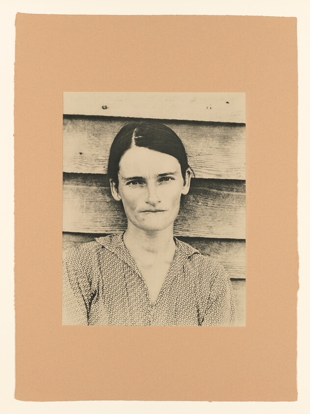 A woman with a neutral expression stands in front of weathered wooden siding.