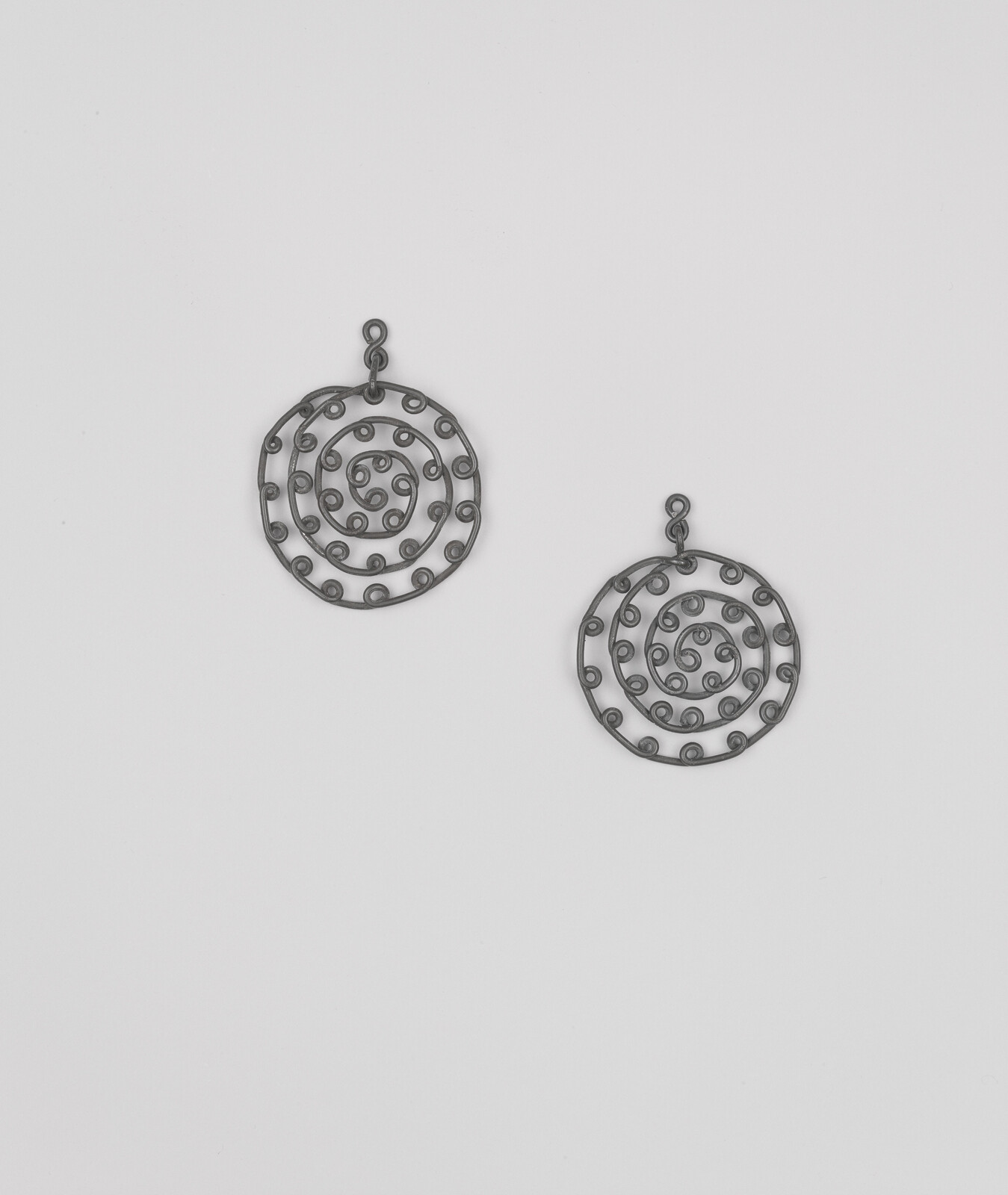 Two round spiral metal earrings with small looped dots on a plain white background.
