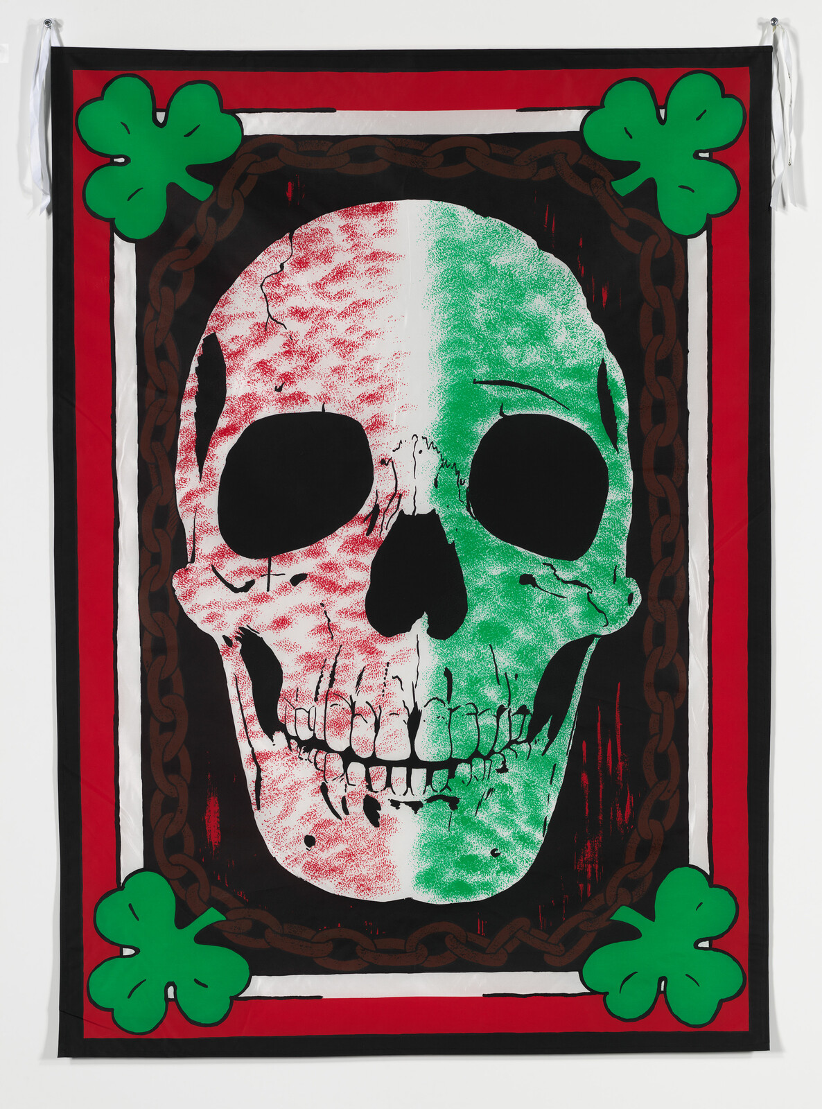 A large skull colored red and green is split vertically on a bordered flag with four green shamrocks.