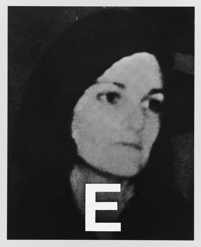 A grainy black and white photo of a woman looking to the side with a contemplative expression. She is wearing a dark hat and a dark top. There is a large, white letter 'E' superimposed over the bottom center of the image.