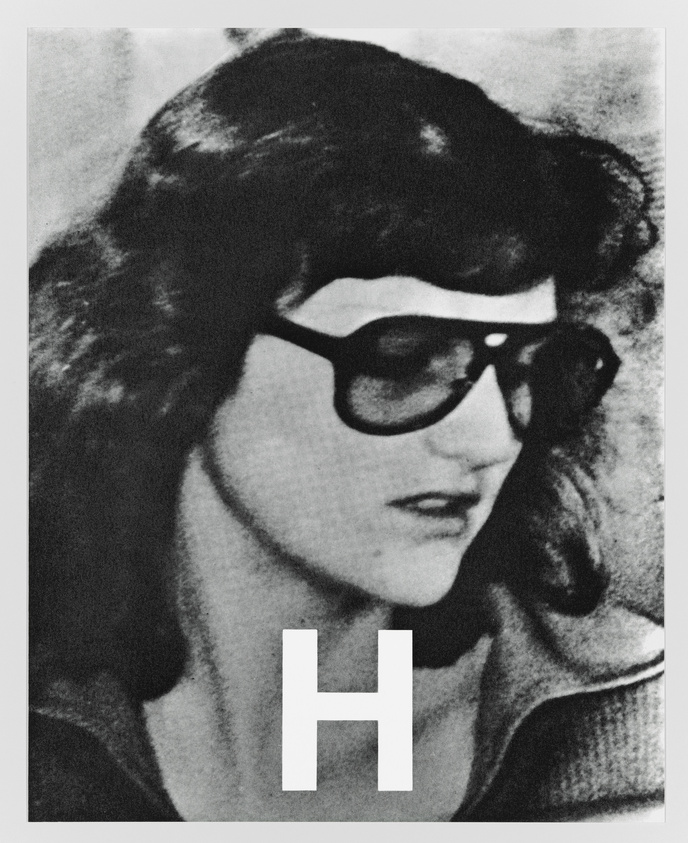 A black and white grainy photo of a person wearing dark sunglasses with a prominent letter "H" superimposed over the image.