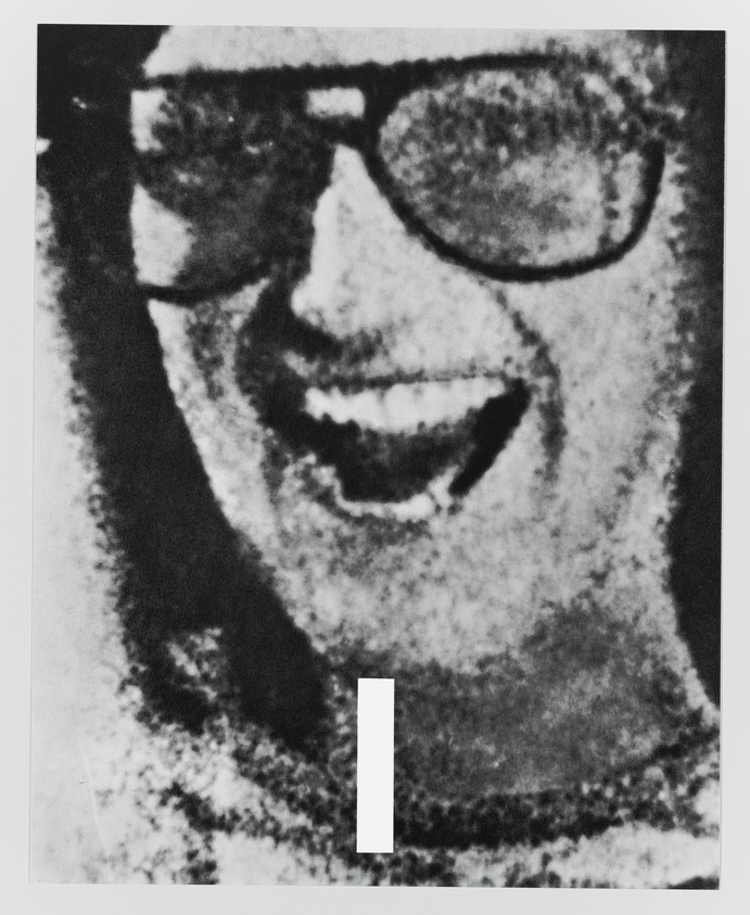 Black and white grainy image of a smiling person wearing sunglasses.