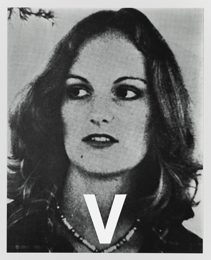 Young woman looking to the side with a large letter V printed over her chest.