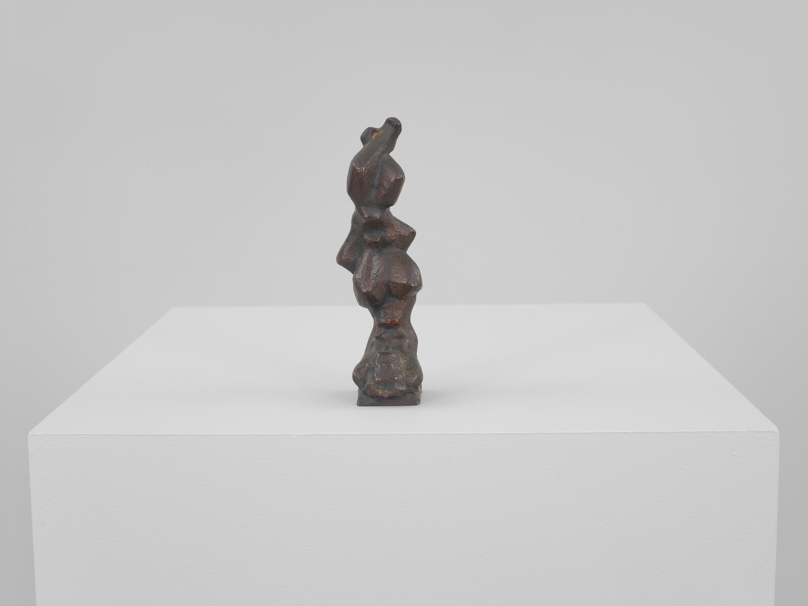 Small dark bronze abstract sculpture with stacked organic shapes standing on a white pedestal.