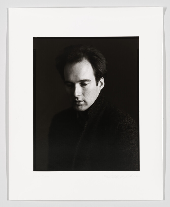 Black and white portrait of a man in profile with a contemplative expression, framed with a white border and signed at the bottom.