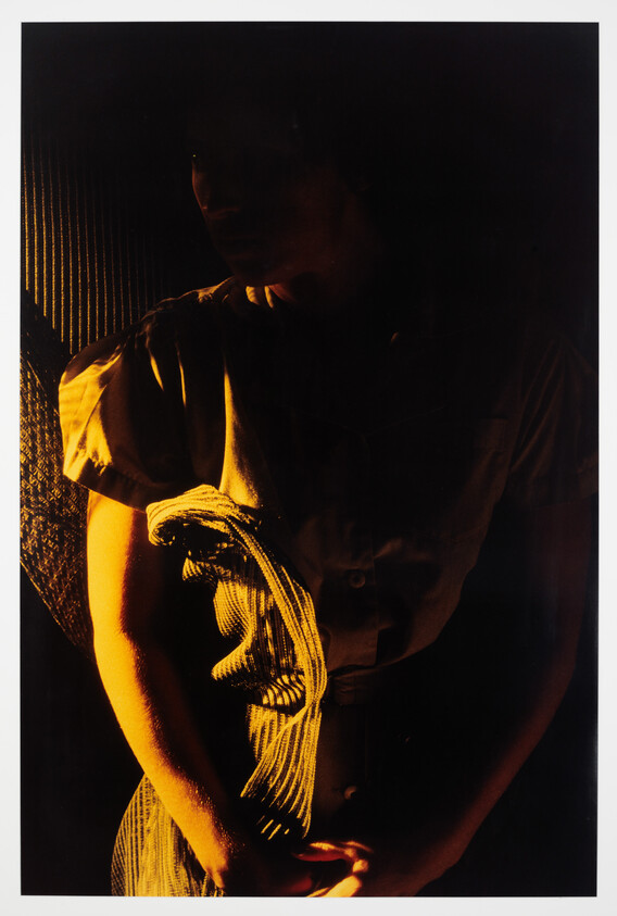 A person stands in dramatic warm light holding striped fabric across their torso.