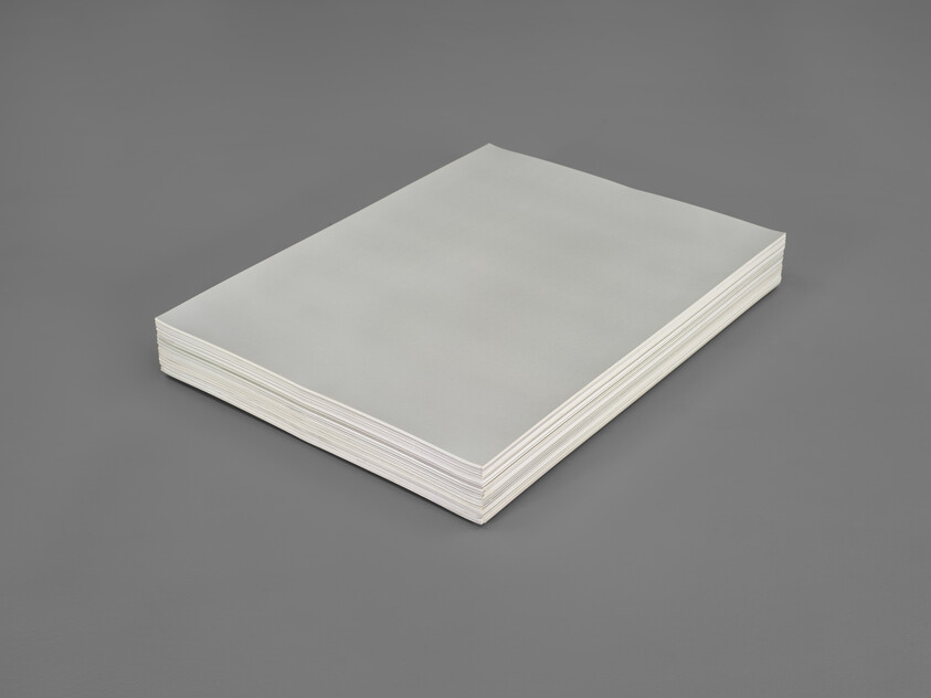 A thick stack of white printer paper rests flat on a gray tabletop.