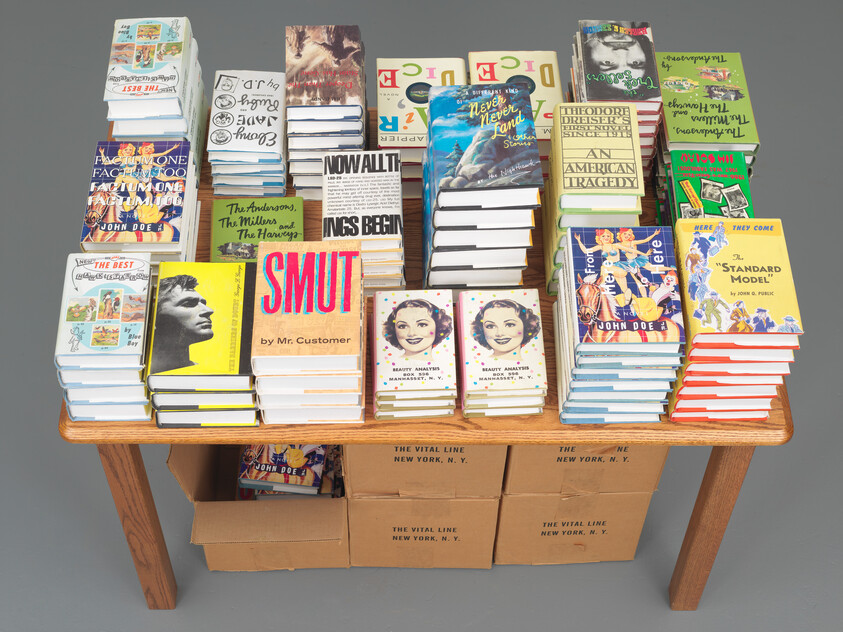 Assorted small paperback books neatly stacked on a wooden table, including one titled SMUT.