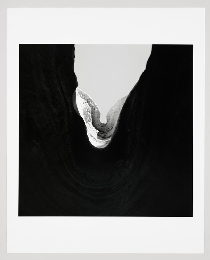 A narrow, light-filled crevice curves like a white crescent inside dark rock.