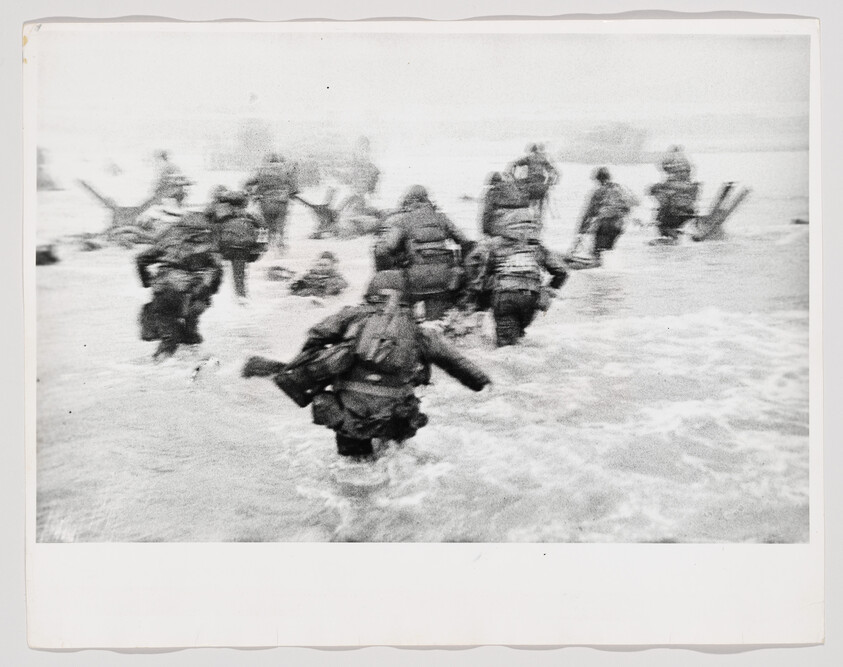 Soldiers wading through rough shallows toward a beach during a wartime amphibious landing.