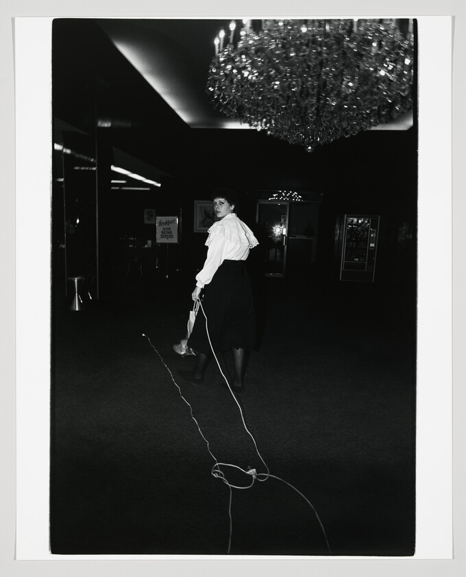 Woman walking through dark lobby looking back while trailing a long cord across the floor.