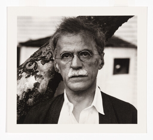 Older man with round glasses and a mustache looking directly at the camera against a tree.