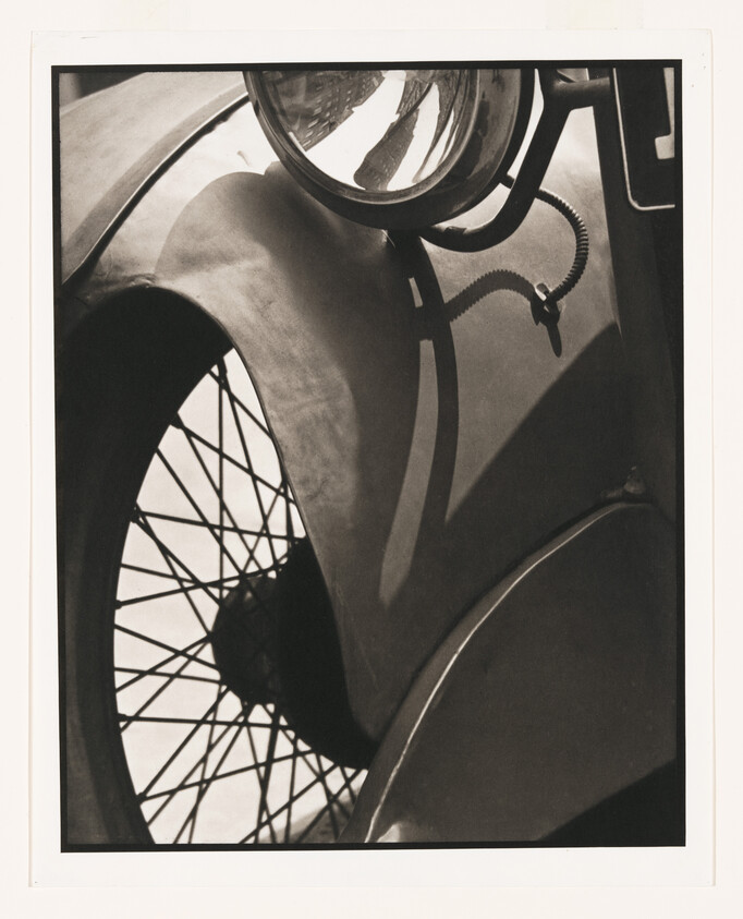 Close-up of a vintage car showing spoked wheel, curved fender, and round headlight.