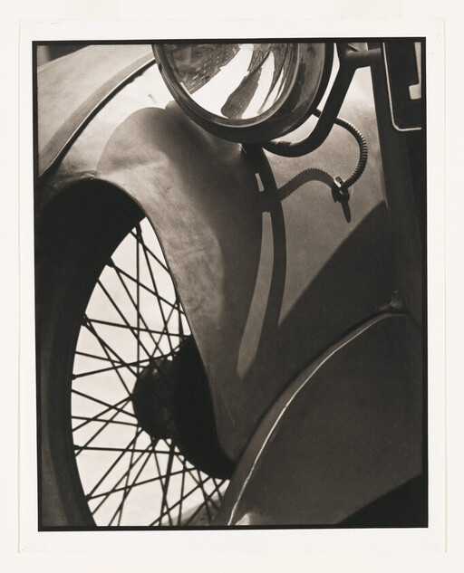 Close-up of a vintage car showing spoked wheel, curved fender, and round headlight.