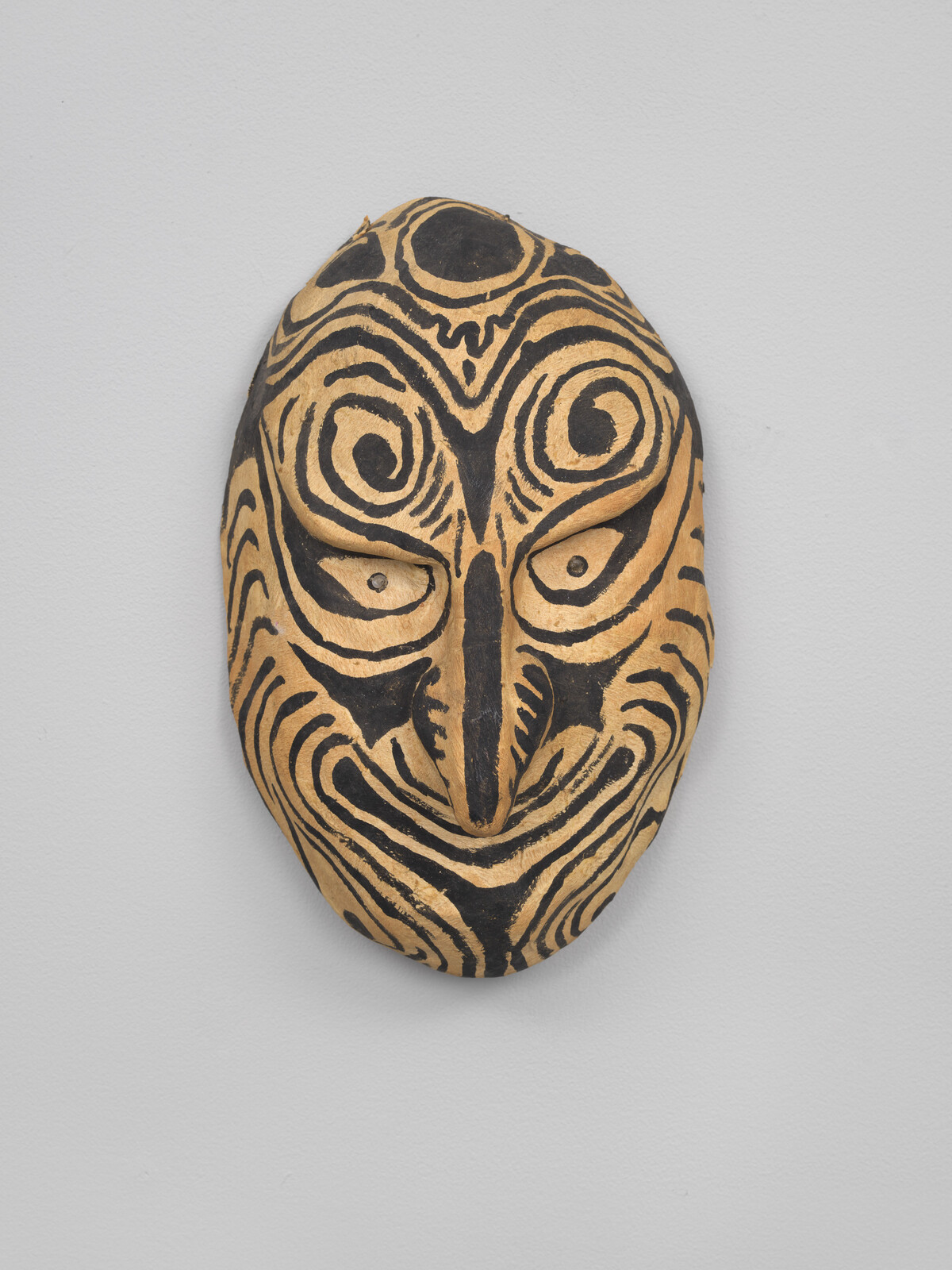 A carved wooden mask with bold black swirl patterns and a long hooked nose.