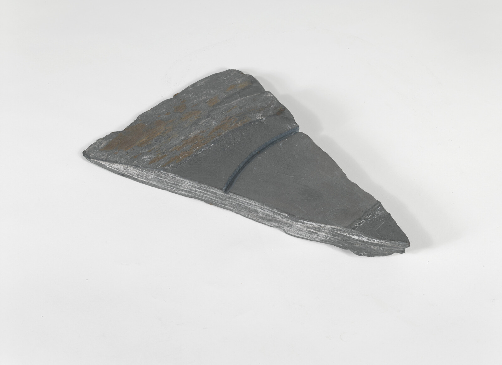A triangular piece of dark gray slate rock with layered edges rests on a white surface.