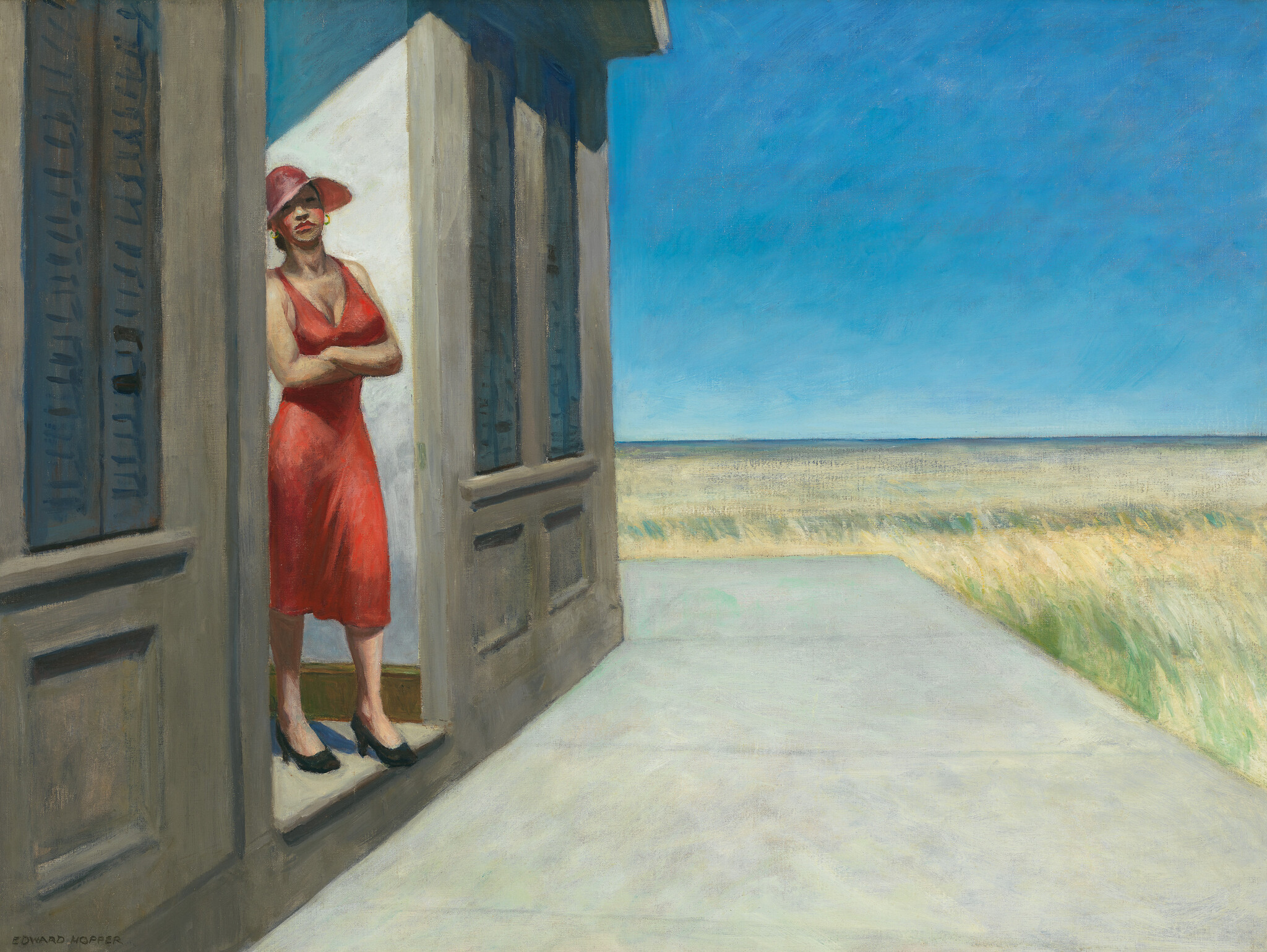 A white woman wearing a a burnt orange dress and sun hat crosses their arms and leans aganist a doorway