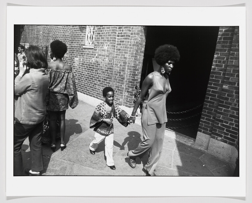 A black woman holds her son’s right hand as she leads him away from a crowd