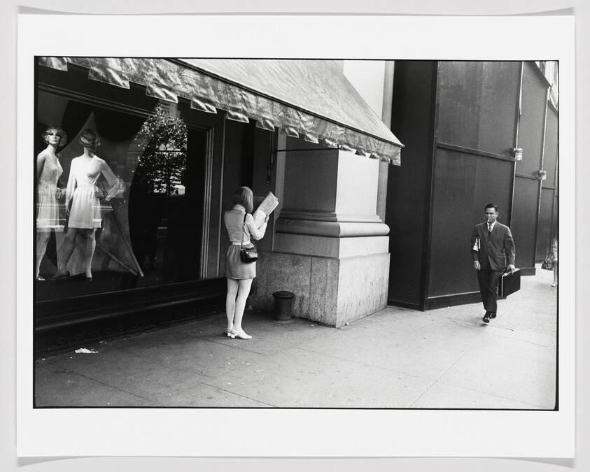 A woman reads a map outside a store window while a man walks by.