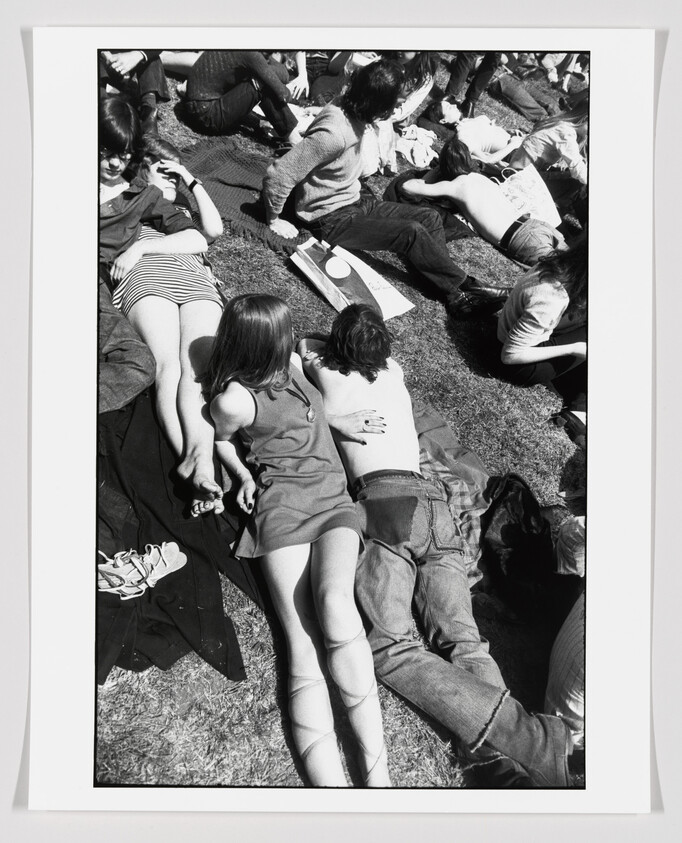 Young people lounging on grass at a park, a couple lying closely together in the foreground.
