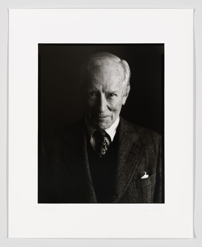 Black and white portrait of an elderly gentleman with a gentle smile, wearing a suit and tie, with a handkerchief in his jacket pocket. The photo is framed with a white border that includes a signature at the bottom.