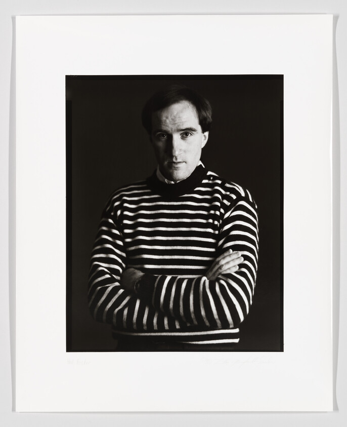 Black and white portrait of a man wearing a striped sweater with arms crossed, looking directly at the camera. The photograph is framed with a white border, and there are signatures at the bottom.