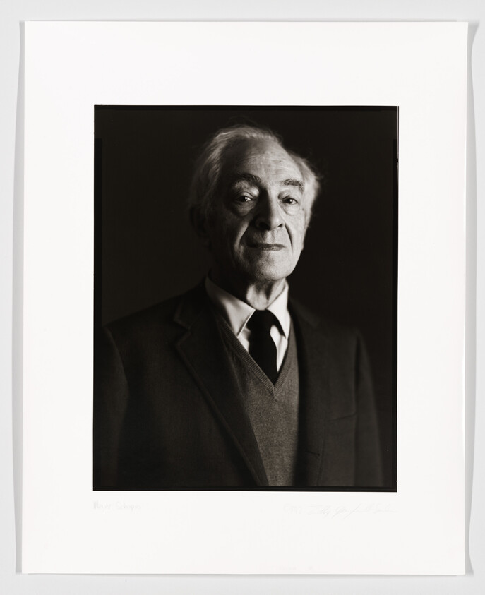 Black and white portrait of an elderly man with a gentle expression, wearing a suit and tie. The photo is framed and includes a signature at the bottom.