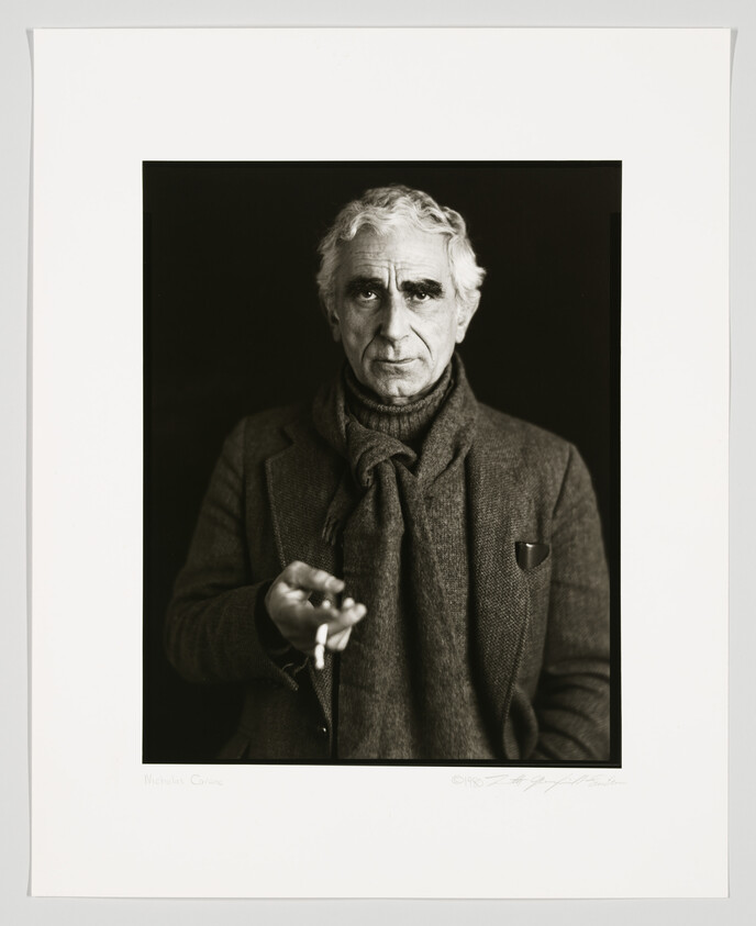 Black and white portrait of an older man with graying hair, wearing a turtleneck and a tweed jacket, holding a pair of eyeglasses. The photo is signed and dated at the bottom.