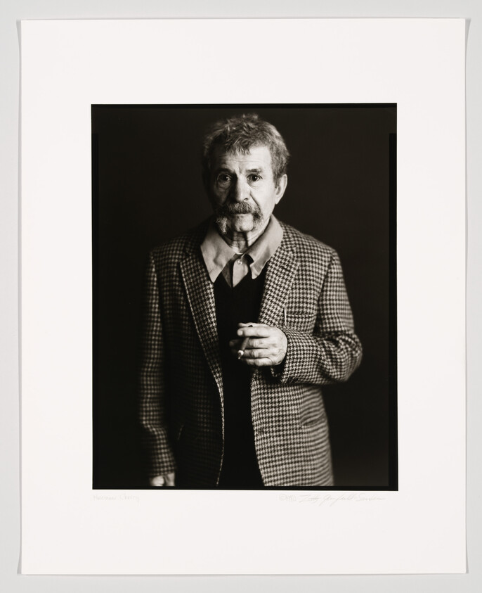Black and white portrait of a mature man with a mustache, wearing a houndstooth jacket and holding a cigarette, framed with a white border that includes a signature and a name at the bottom.