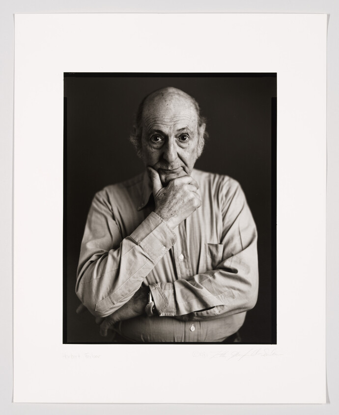 A black and white portrait of an elderly man with a thoughtful expression, resting his chin on his hand. He is wearing a button-up shirt and has a balding head. The photo is framed and includes a signature and a name at the bottom.