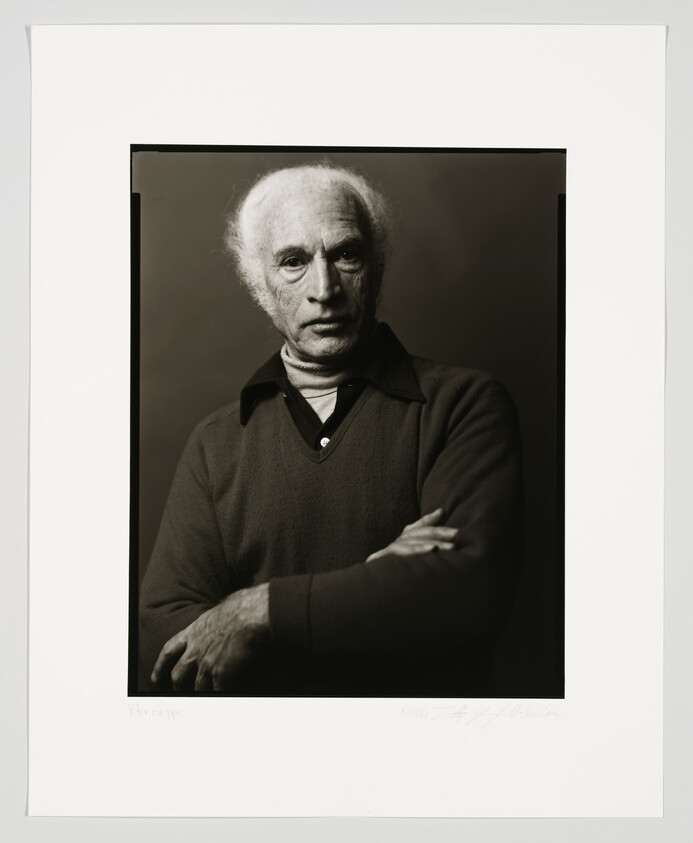 A black and white portrait of an elderly man with receding hairline and thoughtful expression, wearing a dark sweater over a collared shirt, arms crossed. The image is framed with a white border containing a signature and text at the bottom.