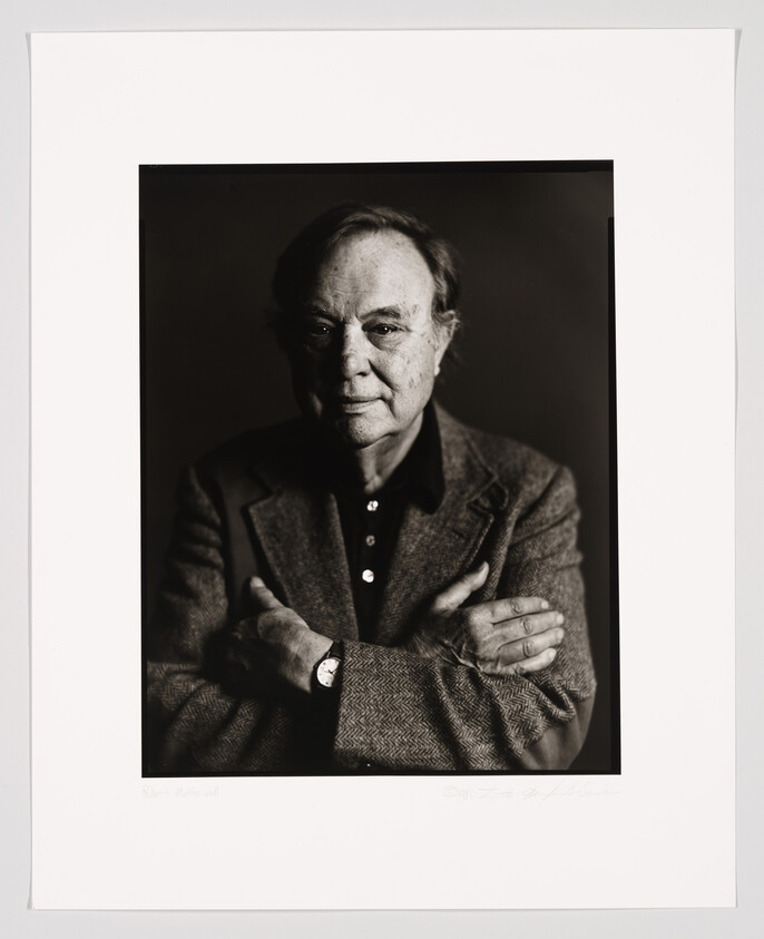 A black and white portrait of an older man with a thoughtful expression, wearing a herringbone jacket and a dark shirt, with his arms crossed. The photo is framed and includes a signature and a name at the bottom.