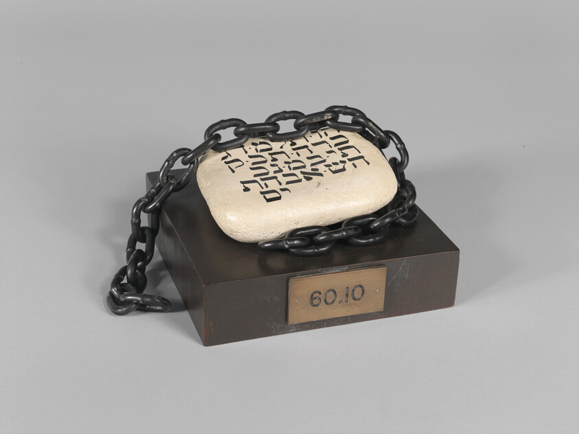 A stone tablet with Hebrew writing bound by heavy chain resting on a wooden display base.
