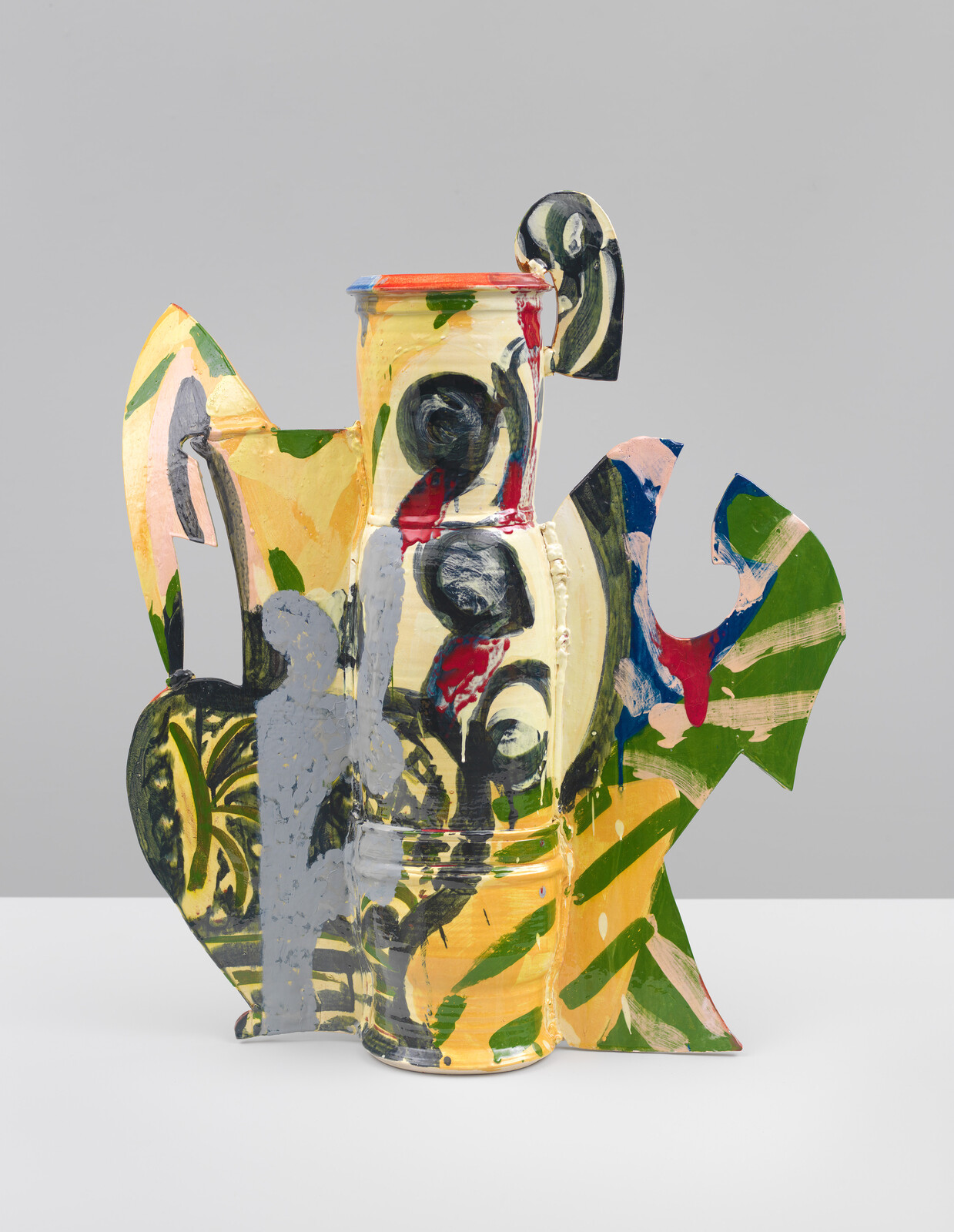 A pitcher-like glazed ceramic with flat, protruding shapes and covered in colorful green, yellow, blue, red, black, and gray brush strokes and patterns.