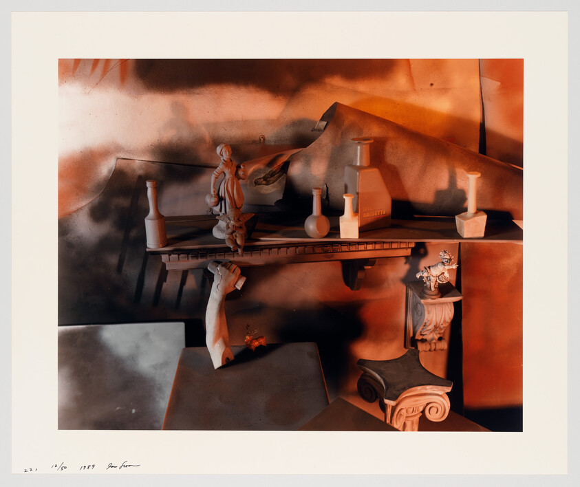 A shelf with small classical sculptures and vases arranged among architectural fragments under warm orange light.