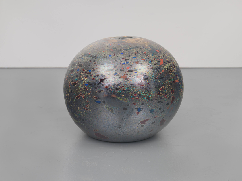 A metallic glass orb covered dotted by blue, orange, and maroon flecks and organic shapes, more concentrated toward the top.