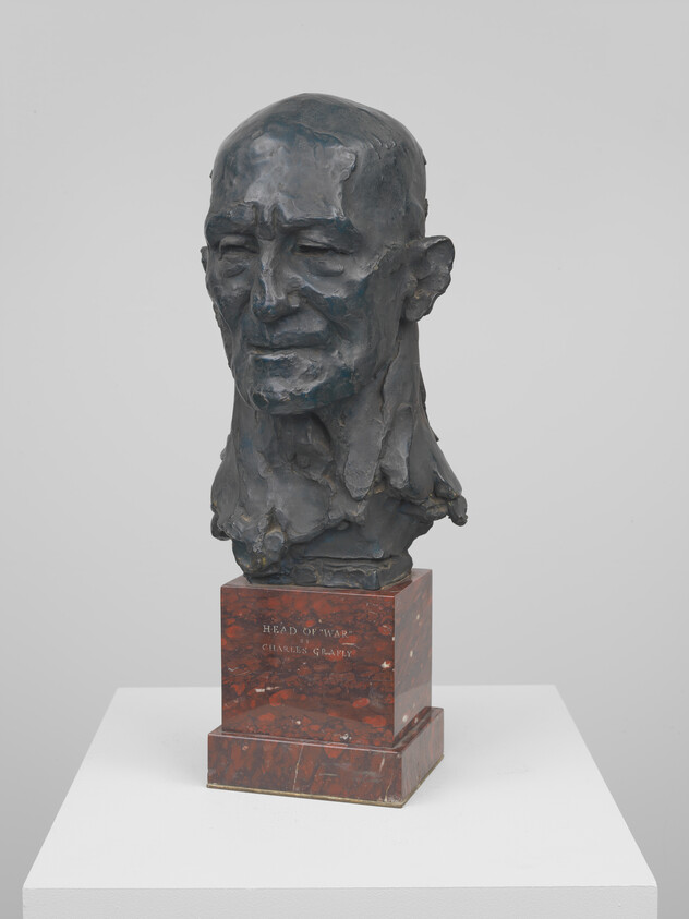 Bronze bust of an elderly man's head mounted on a red marble pedestal.