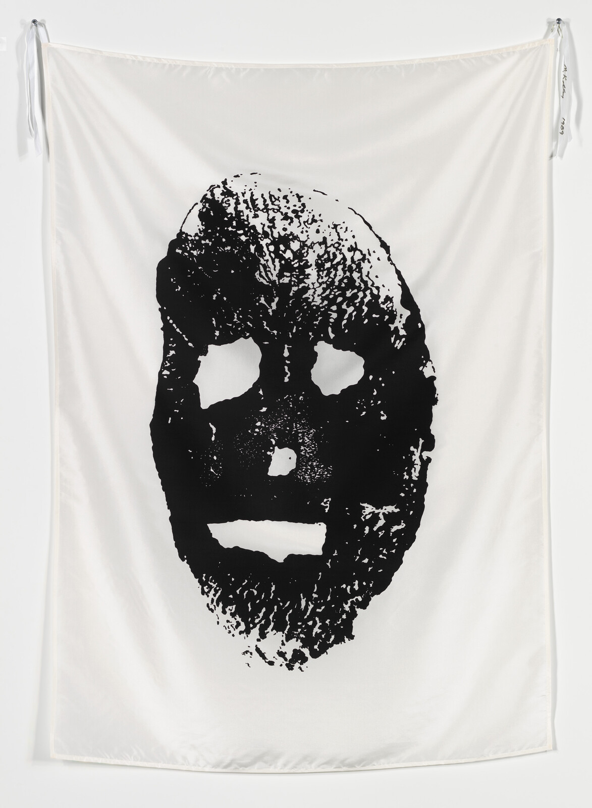Large white fabric hanging with a bold black distressed mask-like face printed in the center.