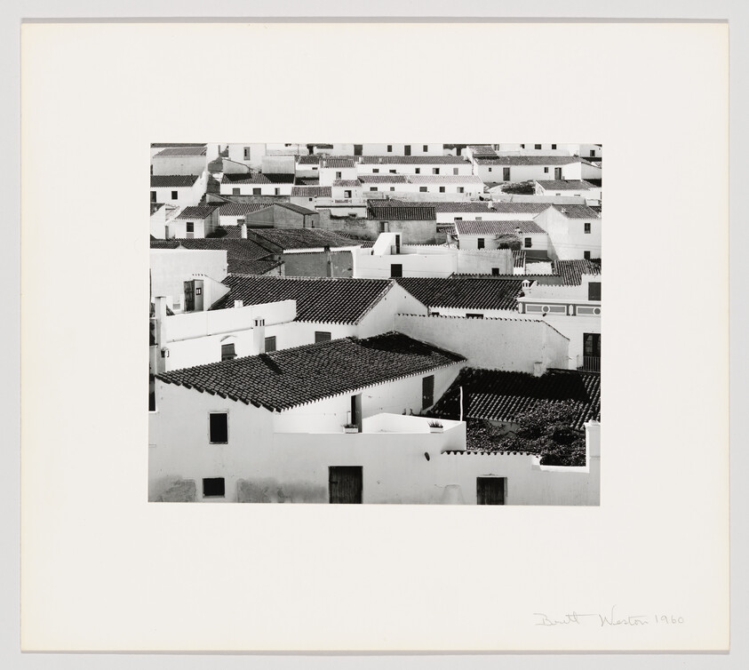 Black and white photograph of a dense cluster of white-washed buildings with tiled roofs, likely in a Mediterranean or similar coastal village, with a signature and date in the lower right corner indicating 1960.